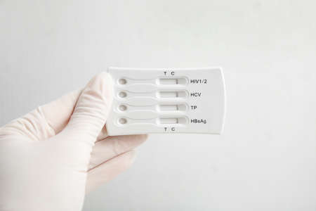 Doctor in gloves holding disposable express test for hepatitis on white background, closeupの写真素材
