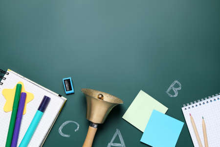 Flat lay composition with golden bell and school stationery on green chalkboard, space for text