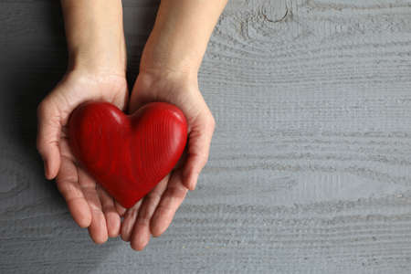 Elderly woman holding red heart in hands at gray wooden table, top view. Space for textの写真素材
