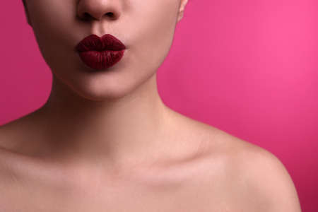 Closeup view of beautiful woman puckering lips for kiss on pink backgroundの写真素材