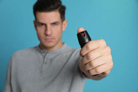 Man using pepper spray against turquoise background, focus on handの写真素材
