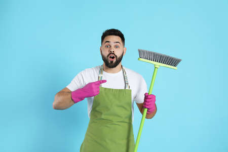 Emotional young man with green broom on light blue backgroundの写真素材