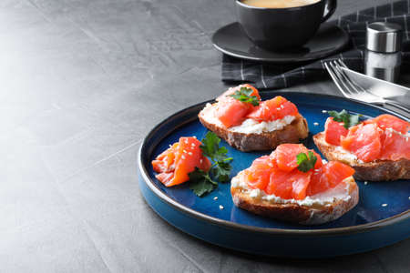 Tasty bruschettas with salmon, cream cheese and parsley on gray table, space for text