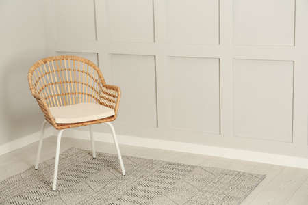 Stylish wicker armchair near light wall in room. Space for text