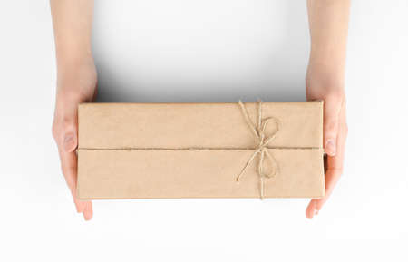 Woman holding parcel wrapped in kraft paper on white background, top view