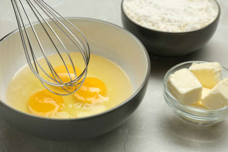 Whisking eggs in bowl on light gray table, closeup