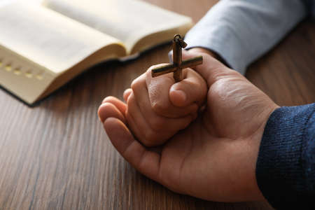 Boy and his godparent holding cross at wooden table, closeup