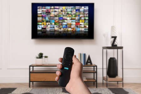 Woman with remote control changing channels while watching TV at home, closeup