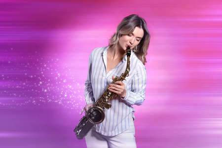 Beautiful young woman playing saxophone on pink backgroundの写真素材
