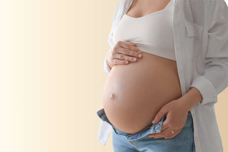 Young pregnant woman touching her belly on beige background, closeup. Space for textの写真素材