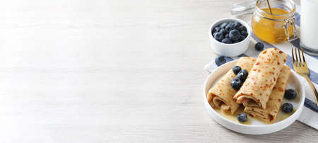 Delicious crepes served with blueberries, honey and milk on white wooden table, space for text. banner designの写真素材