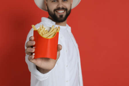 Young man with French fries against red background, focus on hand. Space for textの写真素材