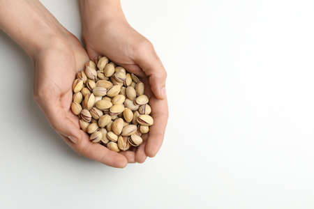 Woman holding tasty roasted pistachio nuts on white background, top view. Space for text