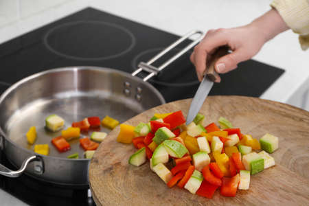 Woman putting cut vegetables into saute pan in kitchen, closeup