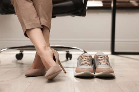 Comfortable sneakers on floor near woman wearing stylish high heeled shoes in office, closeupの写真素材