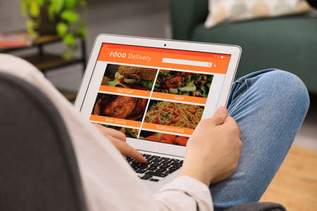 Man using laptop for ordering food online at home, closeup. Concept of delivery service