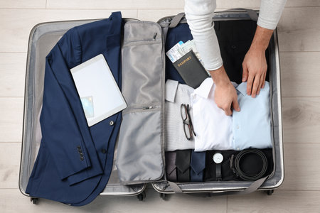 Man packing suitcase for business trip on wooden floor, top viewの写真素材