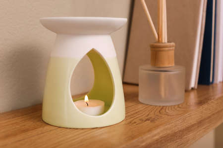 Stylish aroma lamp and reed diffuser on wooden shelf indoorsの写真素材