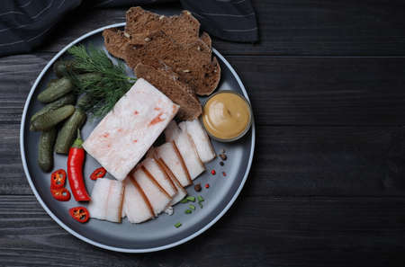 pork fatback with spices, bread and pickled cucumbers on black wooden table, flat lay. Space for...