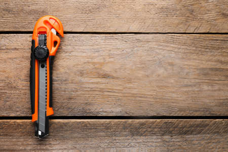 Orange utility knife on wooden table, top view. Space for text