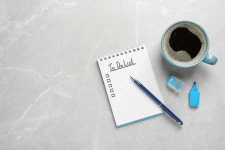 Notepad with unfilled To Do list, pen, marker and cup of coffee on gray marble table, flat lay....