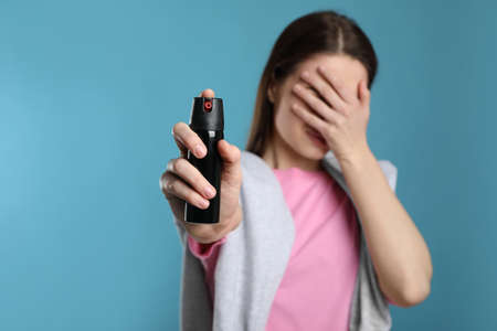 Young woman covering eyes with hand and using pepper spray on light blue backgroundの写真素材