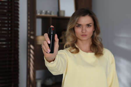 Young woman using pepper spray indoors, focus on hand