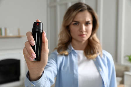 Young woman using pepper spray at home, focus on hand