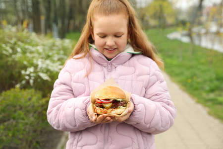 Little girl holding fresh delicious burger outdoors. street foodの写真素材