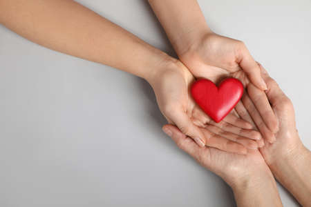 Young and elderly women holding red heart on light gray background, closeup. Space for textの写真素材