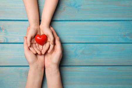 Woman and kid holding red heart in hands at light blue wooden table, top view. Space for textの写真素材