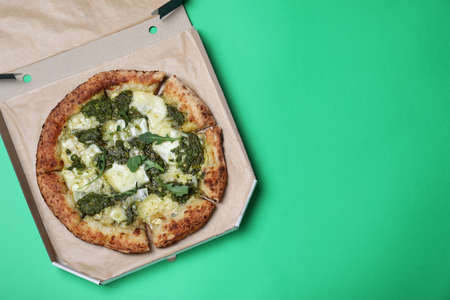 Delicious pizza with pesto, cheese and arugula in cardboard box on green background, top view. Space for textの写真素材