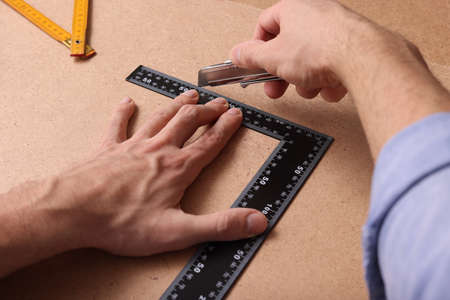 Man cutting chip board with utility knife and ruler , closeup