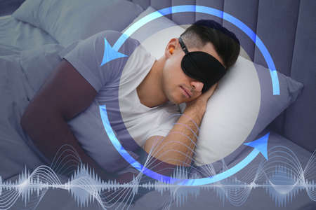 Man with foam ear plugs and mask sleeping in bed. Tips for managing sleep deprivationの写真素材