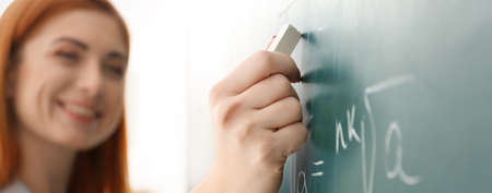Teacher writing on chalkboard in classroom, closeup. banner design