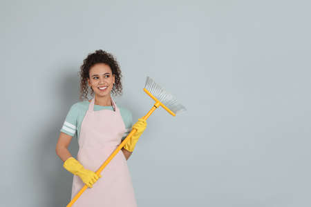 African American woman with yellow broom on gray background, space for text