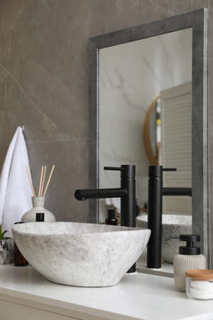 Stone vessel sink with faucet and toiletries on white countertop in bathroomの写真素材