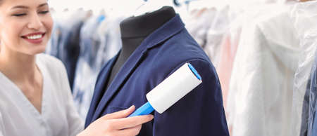 Young woman removing dust from jacket with lint roller, banner design. Dry-cleaning serviceの写真素材