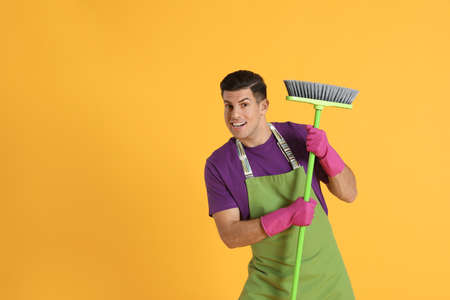 Emotional man with green broom on orange background, space for text