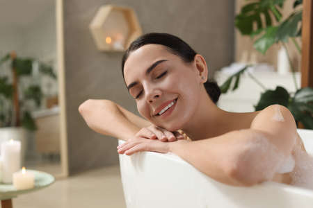 Beautiful young woman taking bubble bath at home