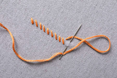 Needle with orange embroidery floss and row of stitches on gray fabric, top view