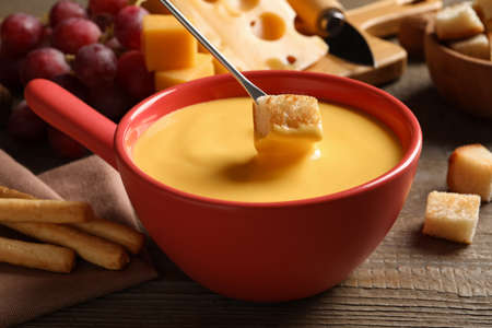 Dipping piece of bread into tasty cheese fondue on wooden table, closeupの写真素材