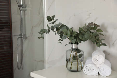 Rolled towels and glass vase with beautiful eucalyptus branches near shower stall in bathroom. interior designの写真素材