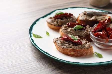 Slices of bread with delicious pate, sun dried tomatoes and basil on wooden table. Space for textの写真素材