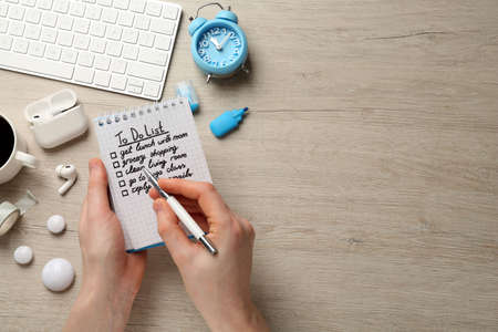Woman checking to do list at white wooden table, top view. Space for text