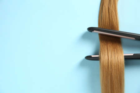 Modern straightener with blonde hair lock on light blue background, top view. Space for textの写真素材