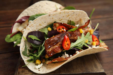 Delicious tacos with fried bacon, vegetables and cheese on wooden board, closeup