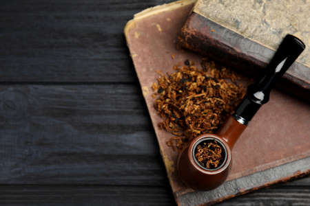 Smoking pipe, dry tobacco and old books on wooden table, top view. Space for text
