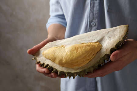 Woman holding piece of ripe durian fruit on gray background, closeup