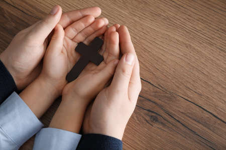 Boy and his godparent holding cross at wooden table, closeup